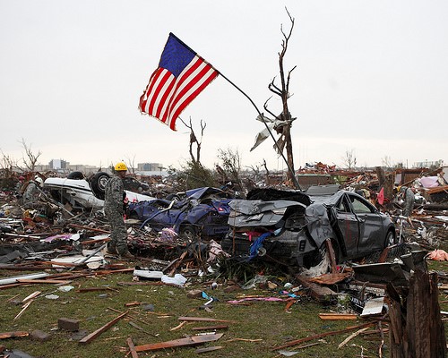 An American flag hangs above wreckage from a tornado. 
